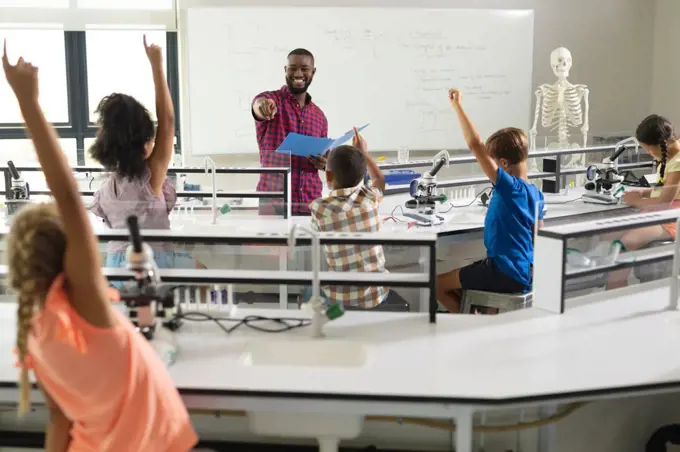 African american young male teacher questioning multiracial elementary students with hands raised. unaltered, education, learning, intelligence, science, stem, teaching and school concept.