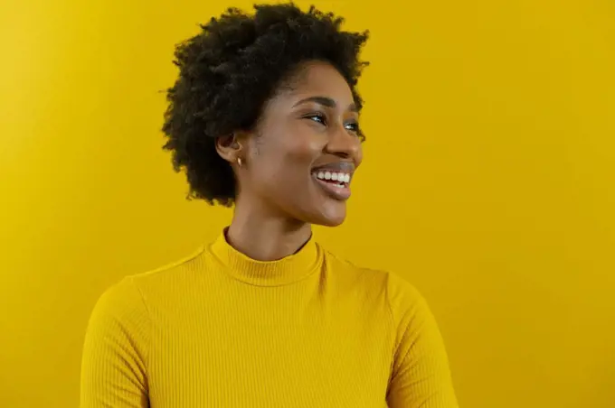 Cheerful young african american businesswoman with afro hairstyle looking away against yellow wall. unaltered, business, people and emotions concept.