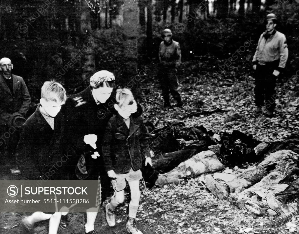 German Civilians Forced - To Exhume Atrocity Victims: A German mother shields the eyes of her son as they walk with other civilians past the row of exhumed bodies outside Suttrop. June 19, 1945. (Photo by U.S. Office of War Information Picture).