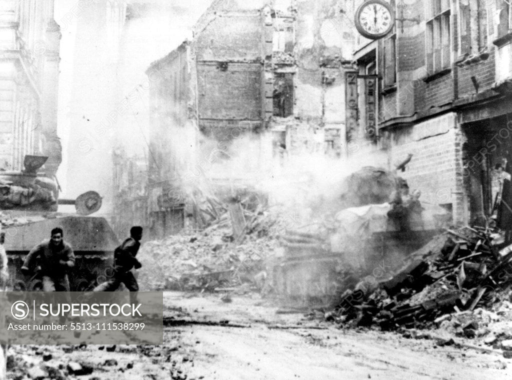 Stock Photo: 5513-111538299 Dramatic Picture of the Battle For Cologne: During fierce fighting in the shadow of the Cologne Cathedral, a U.S. tankman, one leg blown off, lies on top of his was machine after he was blown from the turret by a German shell. While one First U.S. Army soldier (right) rushes to aid the wounded soldier, another runs for stretcher bearers. The wounded solider was the only members of the tank crew to survive the shell hit. The rubble-strewn street is the Komoodientrasse, running from Cathedral Squa