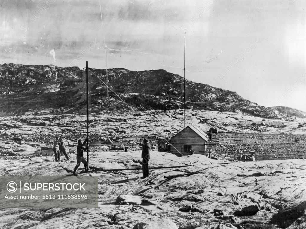 Stock Photo: 5513-111538596 British Arctic Air Route Expedition: A view of the hut built at the Base Camp of the Expedition at Sermilik Fjord, about 80 miles from Angmagsalik. Capt. P. Lemon the wireless operator is seen directing the erection of the second wireless mast. October 25, 1930. (Photo by British Arctic Air Route Expedition Photograph).