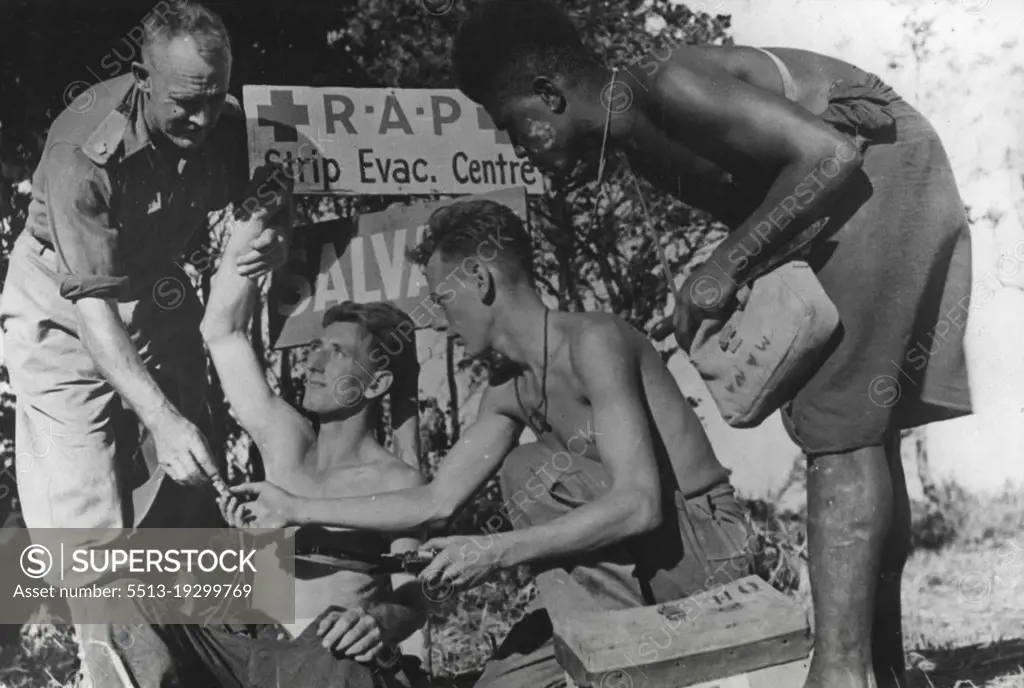 A medical officer from N.S.W. attends a wounded Victorian soldier while Pte. W. Gilbert of Randwick, N.S.W., and Manaze a Markham Valley Native, assist him. November 2, 1943.