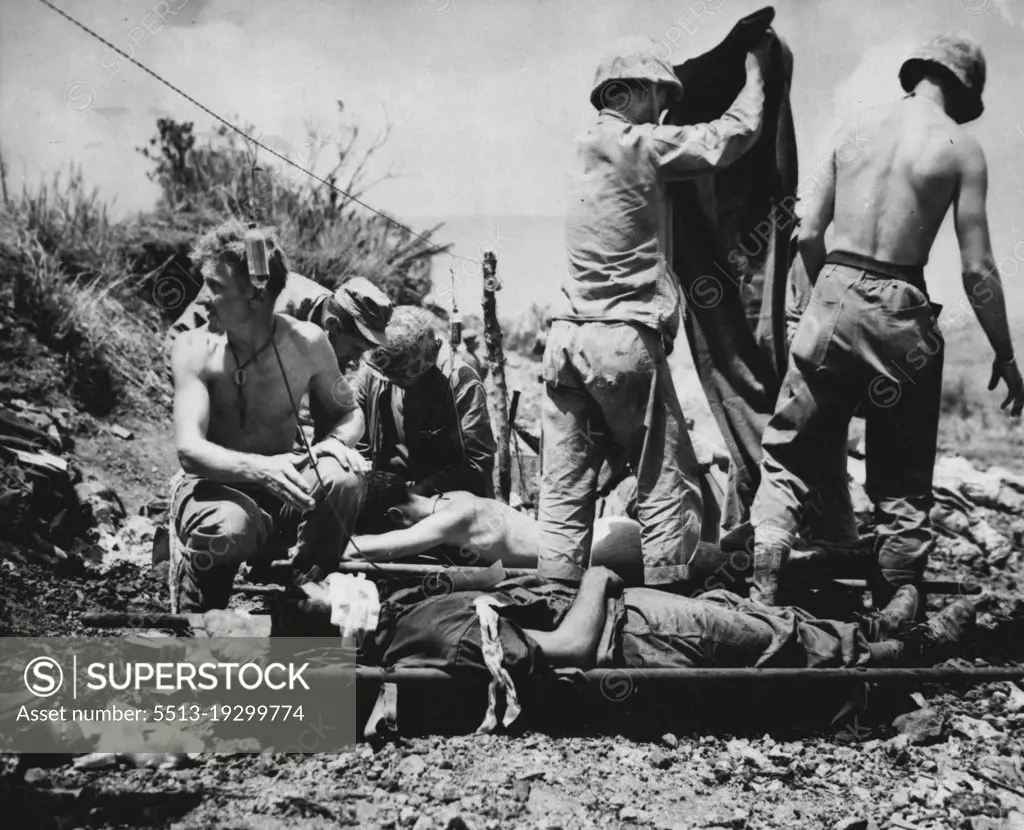 Aid For Wounded On Okinawa -- Wounded troops on Okinawa are given first aid at a forward station. Corpsmen have strung a wire to hold bottles of blood plasma. May 30, 1945. (Photo by Associated Press Photo).