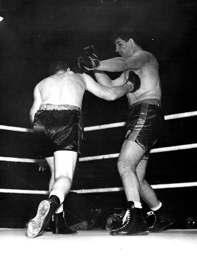 "Potty" Lucky To Draw Parker sinks a hard one to the South African Giant's body. Ewart Potgieter, the seven-foot-two South African heavyweight now boxing in England, was lucky to get away with a draw last night in his match at Harringay against Canada's James J. Parker. Parker seemed to gain points in round after round, with lefts and rights to the body and head. But Potgieter seemed unaffected and the referee called it a draw. Many spectators felt "Potty" lucky to be able to called himself "undefeated in 10 professional bouts" and that he needs much more experience and training before trying to wake on better fighters that he has done so far. November 15, 1955. (Photo by Paul Popper Ltd.).