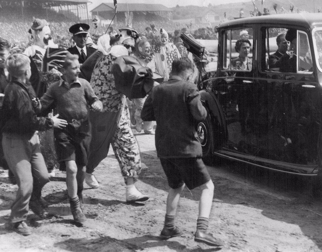 Dunedin (NZ) police had a hard task clearing the way for the Royal car, as children and adults mobbed it when the Queen and Duke of Edinburgh attended a reception. Clowns assisting in the entertainment at the reception helped police push back the crowd. January 30, 1954.