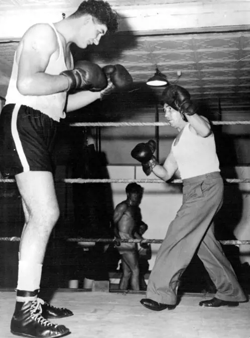 Potgieter tower over his trainer, former South African bantam champion Johnny Hold at they shape up in the gymnasium. February 18, 1955.