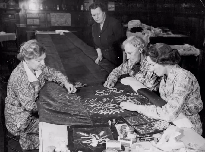 Queen's Coronation Robe Embroidered in London. Working on the embroidery of the Queen's Coronation robe at the Royal School of Needlework today. At left of table is Miss Violet Wise of Finchley, who worked on the Queen Mother's Coronation robe. Standing at right is the Head of the Workroom, Miss Rhoda Rasey (of Kingsbury). Miss M. Evans (Kensington), who also worked on the Queen Mother's robe; and Miss Margaret Bartlett of Leatherhad (nearest *****). February 11, 1953.