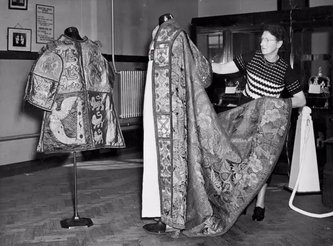 Kent Sees Coronation Robes and Crown Jewels Replicas Mrs. M.M. Beaumont of Sittingbourne, wife of the Secretary to St. Johns Order and Area Commander prepares the Coronation cope of the the Archbishop of Canterbury. On left is the tabard of Sir Gerald Woods Wollaston, KCB, KCVC, Norroy and Ulster King at Arms. Viscountess Allerby today opened an exhibition of Coronation robes and or replicas of the Crown jewels at Dunk memorial Hall, Maidstone, Kent, held by the council of the Order of St. John to raise funds for their cadets. The exhibition will be held also at Canterbury and Tunbridge wells. October 04, 1952. (Photo by Fox Photos).