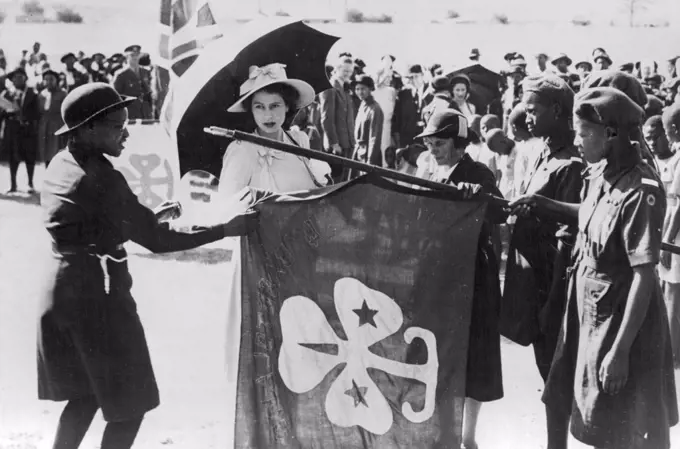 Over 70,000 Basuto Greet Royal Family -- H.R.H. Princess Elizabeth examines a banner at a Parade of native Girl Guides held at Maseru in honor of the Royal Visit. Between 70,000 and 90,000 Basuto assembled in and around Maseru to welcome the Royal family, Many of the natives had trekked for more than a week, camping by the wayside, in order to be in capital to pay homage to their king. March 17, 1947. 