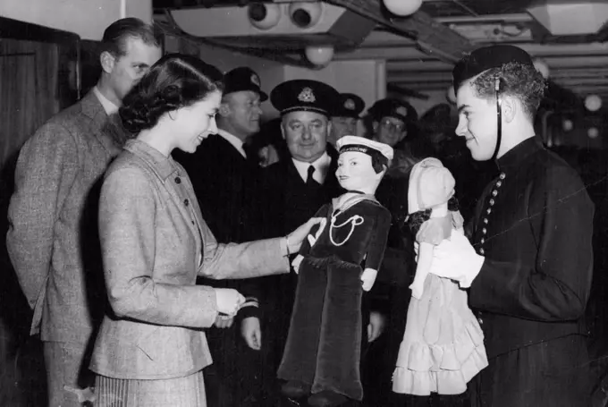 The Princess During Atlantic Crossing Special Pictures By S. Devon -- George Newcombe, Senior Beld boy on the ship, Presenting to Princess Elizabeth two dolls for Princess Anne and Prince Charles which were subscribed for be the ship's company. Also in the picture are the Duke of Edinburgh and Capt. C. E. Duggan, master of the "Empress of Scotland". Photographers released today show Princess Elizabeth during her trip from Canada on the S.S. "Empress of Scotland" in which she landed at Liverpool yesterday. November 18, 1951. (Photo by Paul Popper).