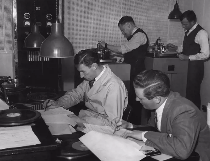 Finally record of episode is cut. Neville Merchant (L) Production Panel Operator puts in incidental music & sound effects while Producer Jacklin follows dialogue on script. In background actual cutting machines are in process of recording. Back left, Bill Dukes, technician, cuts acetate record while Engineer Burt Munnings cuts process record. November 4, 1944.