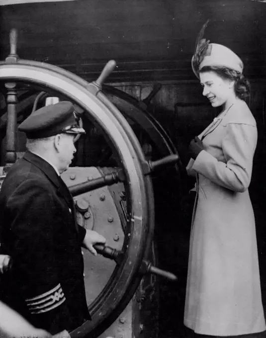 Princess Takes The Wheel - H.R.H. Princess Elizabeth takes a close look at the great steering wheel of the New Zealand four masted barque Pamir, during her visit with the Duke of Edinburgh to the ship in Shadwell Basin. The ship's master Capt. H. Collier is explaining the mechanism,- to-day (Wednesday). March 3, 1948. (Photo by Reuterphoto).