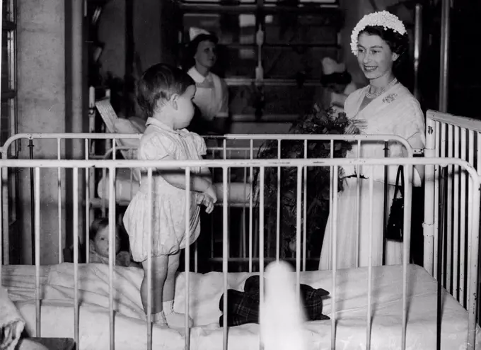 Queen Meets Hospital Baby - London: Wearing a Summer dress of Pleated white chiffon, and a tiny East to West cap of white ***** the Queen stops to talk to Reginald Parker, aged eighteen months (from Rochester, Kent) while visiting the Great Ormond Street (London) hospital for Children. July 23, 1952.