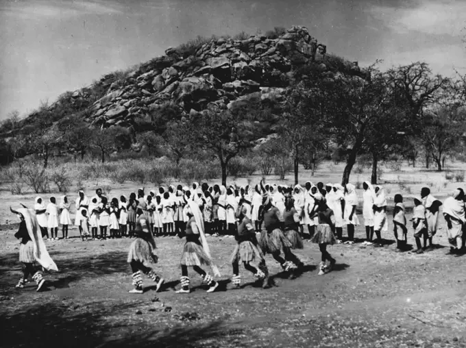 Sudanese Girls Train To Be Teachers.
They Learn In Grass Hut Classrooms Until New College Is Ready.
Boys from a nearby Training School dance a traditional Nuba dance (wearing bulls' horns), watched by girls from the Teachers' Training Centre. May 14, 1953. (Photo by Central Office Of Information).