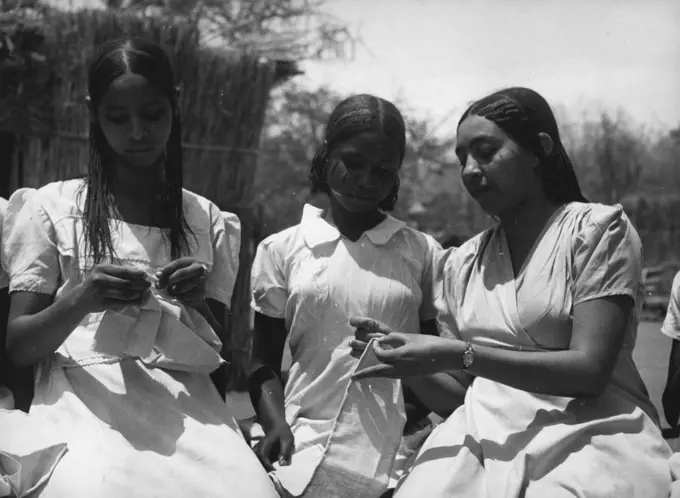 Sudanese Girls Train To Be Teachers.
They Learn In Grass Hut Classrooms Until New College Is Ready.
The sewing class for the girl teacher trainees is held outside between grass-hut classrooms. Main seldom falls in billing and only during the wet season. May 14, 1953. (Photo by Central Office Of Information).