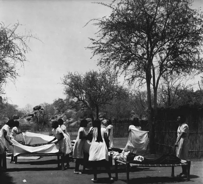 Sudanese Girls Train To Be Teachers.
They Learn In Grass Hut Classrooms Until New College Is Ready.
making beds out in the open is easier than inside the grass hut. Sleeping in the open is a common practice in the Sudan, especially in the hot season when temperatures, even at nights, can be over 100 degrees. May 14, 1953. (Photo by Central Office Of Information).