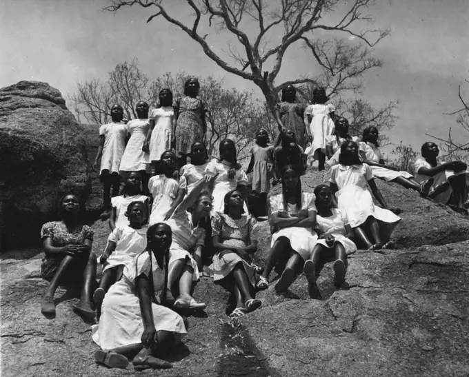 Sudanese Girls Train To Be Teachers.
They Learn In Grass Hut Classrooms Until New College Is Ready.
Resting at the summit of the rocky hilltop this group of girls combines a geography less in with P.T. and listen to the teacher, Miss Anne Gosling (centre) pointing out features on the plain below. May 14, 1953. (Photo by Central Office Of Information).