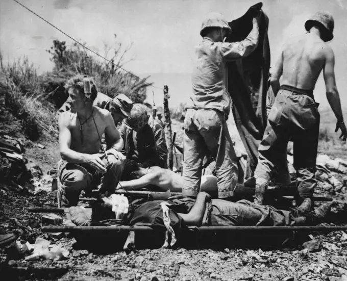 Aid For Wounded On Okinawa -- Wounded troops on Okinawa are given first aid at a forward station. Corpsmen have strung a wire to hold bottles of blood plasma. May 30, 1945. (Photo by Associated Press Photo).