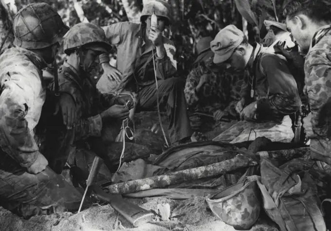 A Wounded Marine Gets Blood...Despite sniper fire, hospital corpsman and Marine Raider doctor gather around a wounded Marine on Bougainville to administer blood plasma. This Marine was hit attempting to knock out an enemy machinegun nest. This medical attendants shown here are, left to right: Pharmacists Mate Second Class Pete A. San Miquel (head turned) 20, of Mays Landing, N.J.; Pharmacists Mate Second Class Sidney G. Jeffcoat, 19, of Big Spring, who holds a plasma unit; Lieutenant Joseph G. Humbert, (M.C.) USN, of Stewartsville, N.J.; Marine Raider surgeon here preparing a second plasma unit, and Chief Pharmacists Mate Claude E. Oreech, 25, of La Grange, N.C. February 13, 1944. (Photo by Official U.S. Marine Corps Photograph).