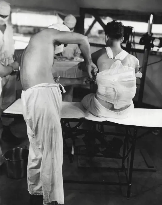 Physician at a Marine Hospital in the Solomons prepares to remove the bandage from a patient with a shrapnel wound in his back in order to dress the wound. January 12, 1944. (Photo by Official U.S. Navy Photograph).