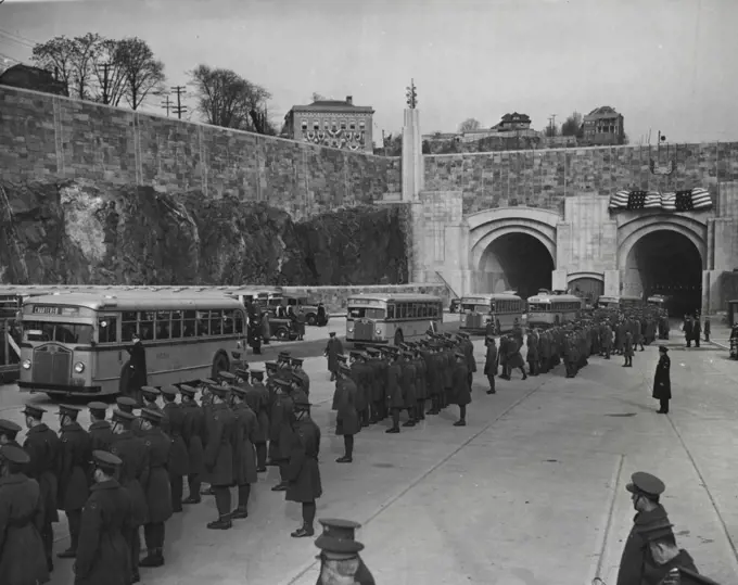 Parade Opens New Manhattan Gateway --  Here is a parade of buses emerging from the new Lincoln Tunnel connecting New Jersey with mid-town New York City as dedication ceremonies for the south tube were held Dec. 21. Shown here is the Jersey portal of the new Subhudson vehicular route. Troops are lined up along the roadway as the buses which carried buses which carried 1,500 through the tunnel emerge. December 21, 1937. (Photo by Associated Press Photo).