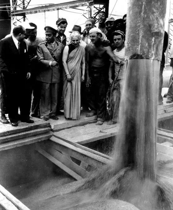 Wheat For India -- Madame Pandit, (center), India's Ambassador to the U. S., watches last of 336, 000 bushels of wheat being funneled aboard Liberty ship, John Chester Kendall, here today, following ceremonies in which Madame Pandit accepted first shipload of U.S. Wheat for her famine- stricken country. Wheat is first of 2 million tons bound  for India. Others shown with Madame Pandit are unidentified. June 19, 1951. (Photo by AP Wirephoto).