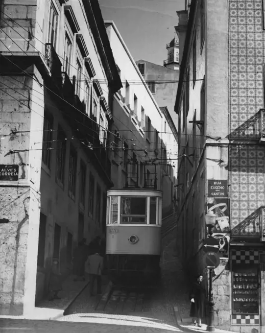This is one of the six funicular (cable railway) lines connecting modern Lisbon with the ancient Alfama quarter of the city, which sits atop seven hills. Note the steep grade it climbs in this narrow street. The house at right has the colored tile decorations that are so prevalent in Lisbon. April 22, 1955. (Photo by United Press).