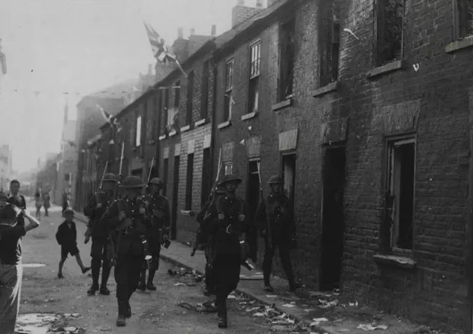 Serious Rioting in Belfast -- The scene of devastation in Little York Street, Belfast, following the rioting. Men of the Fighting Patrol of the Boarder Regiment are seen patrolling the street.Serious rioting broke out in the York Street Area of Belfast on Saturday, when a detachment of Orangemen, who were returning from Belfast's great "Twelfth of July" (Battle of the Boyne) demonstration, were fired on. Two persons were killed and many others wounded. July 16, 1935. (Photo by Topical Press).