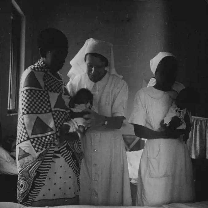 The Matron on her morning rounds stops at the maternity ward to see the twins. With her is Nurse Tepi, a mid-wife trained at the Zanzibar Hospital. The mother is the wife of a Zanzibar farmer. September 19, 1951. (Photo by British Official Photograph).