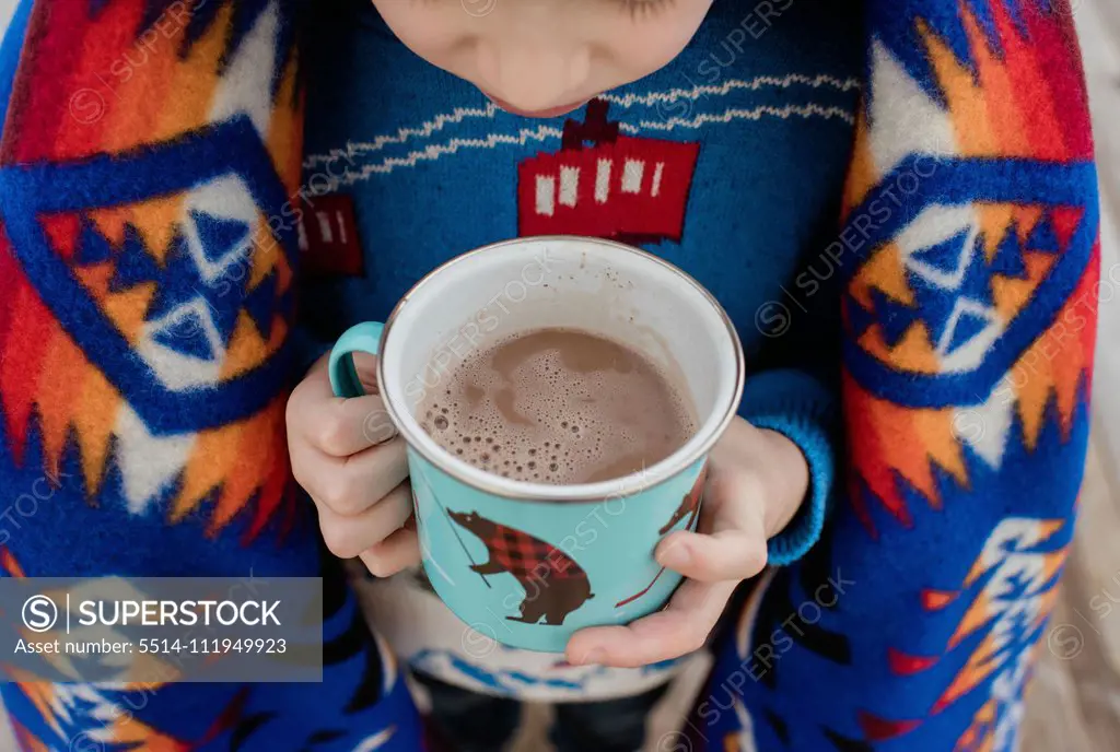 sky view of a boy wrapped in a blanket holding a hot chocolate outside