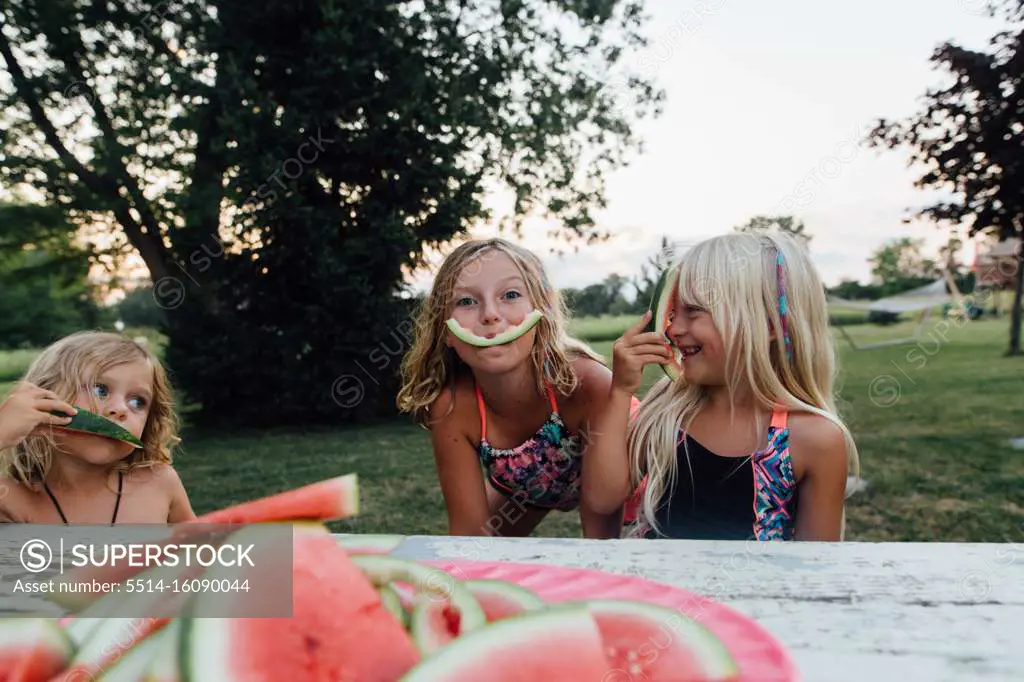Young kids being silly while eating watermelon outside in the summer