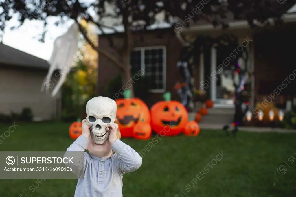 Toddler holding skeleton head in front of halloween decorations