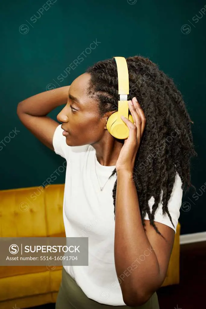 Black stylish student woman holding yellow earphones front green wall