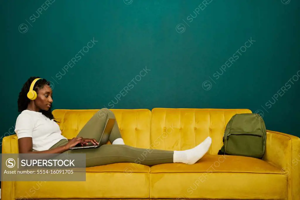 Afroamerican student laying at a yellow sofa front a dark green wall