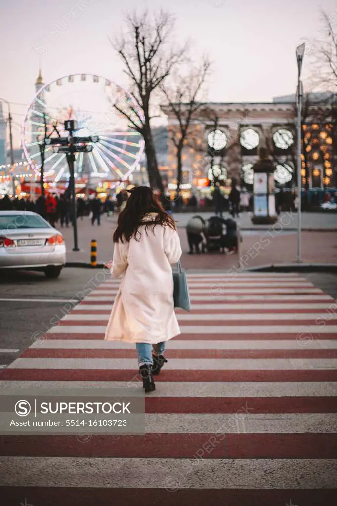Rear view of young woman crossing road in city in winter