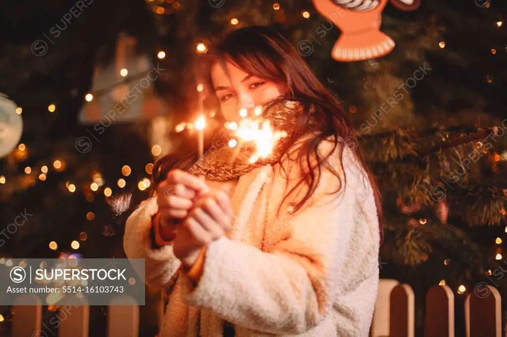 Teenage girl holding sparklers standing by Christmas tree at night