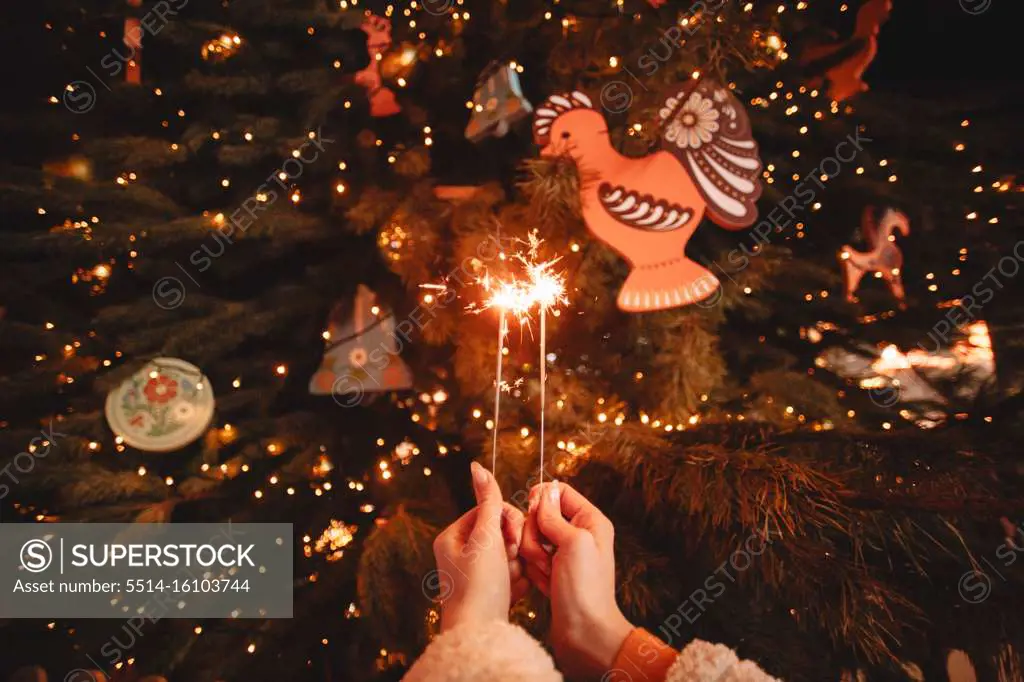Female hands holding sparklers in front of luminous Christmas tree
