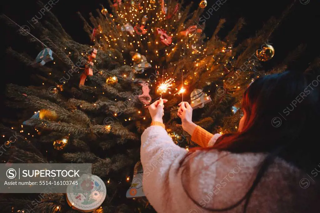 Teenage girl holding sparklers standing by luminous Christmas tree