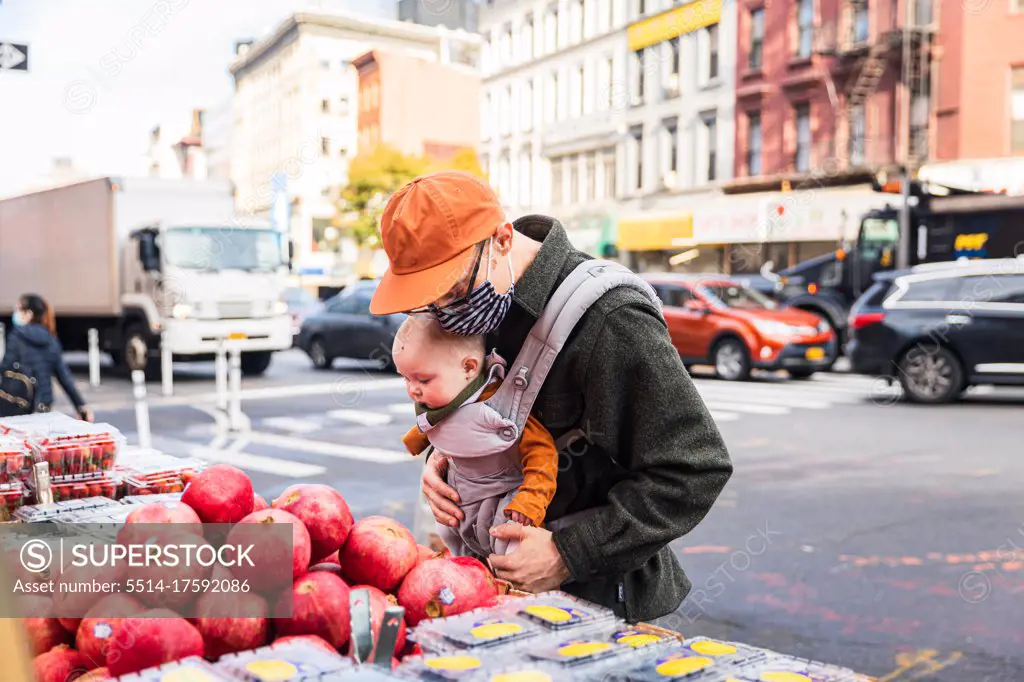 Father with baby girl buying pomegranates on street in city during coronavirus pandemic