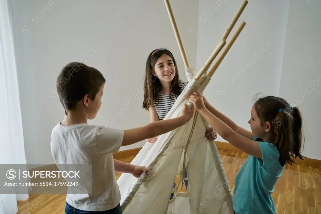 Children putting the sticks to build a teepee tent inside their house. Creativity concept