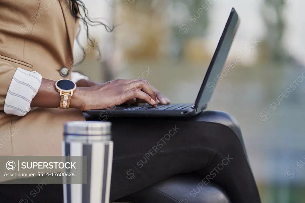 detail of a black woman in a brown suit working on her laptop sitting on the street