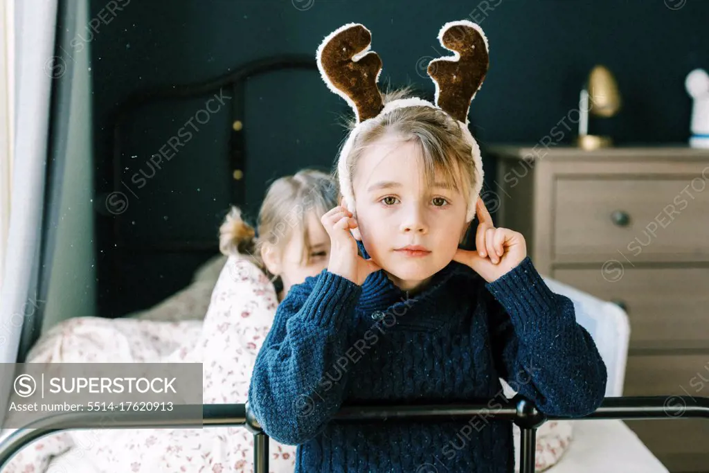 Little boy in a blue knit sweater with a reindeer hat in room on bed
