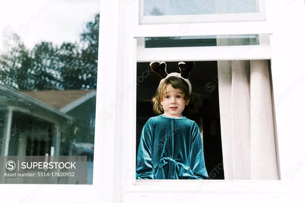 Little girl looking out window with reindeer antlers and a funny face