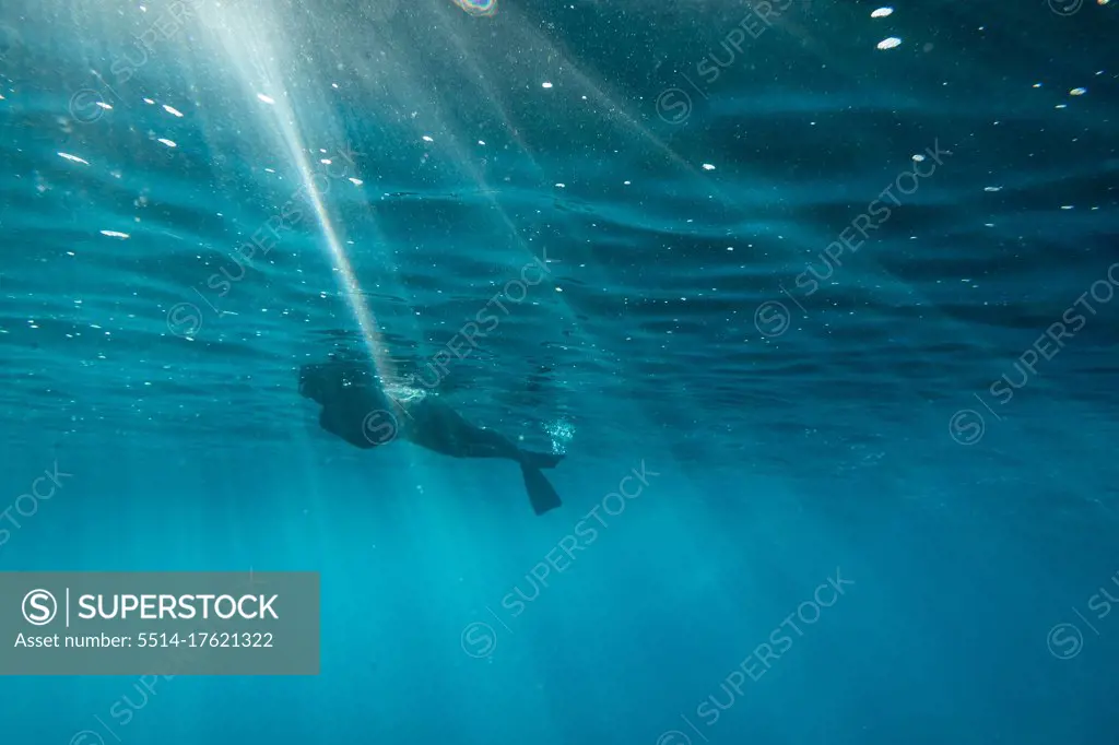 Female snorkels through light streaks at the surface of oahu ocean