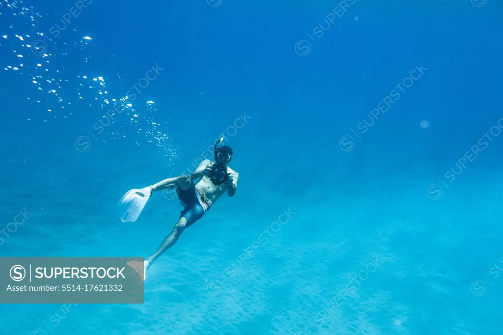 A male snorkeler shoots photos underwater in oahu, hawaii