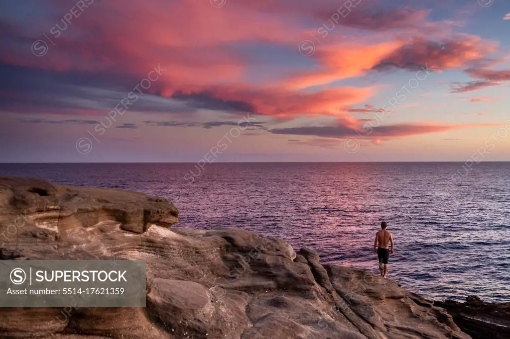 Male stands on cliffs over the ocean at sunset in hawaii