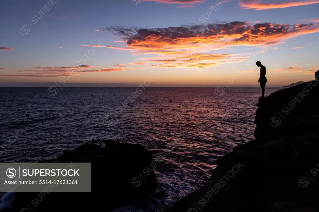 Cliff diver prepares to jump into the ocean at sunset in hawaii