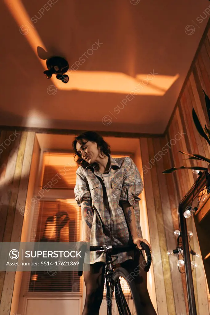 Woman in shirt stands at home with bike