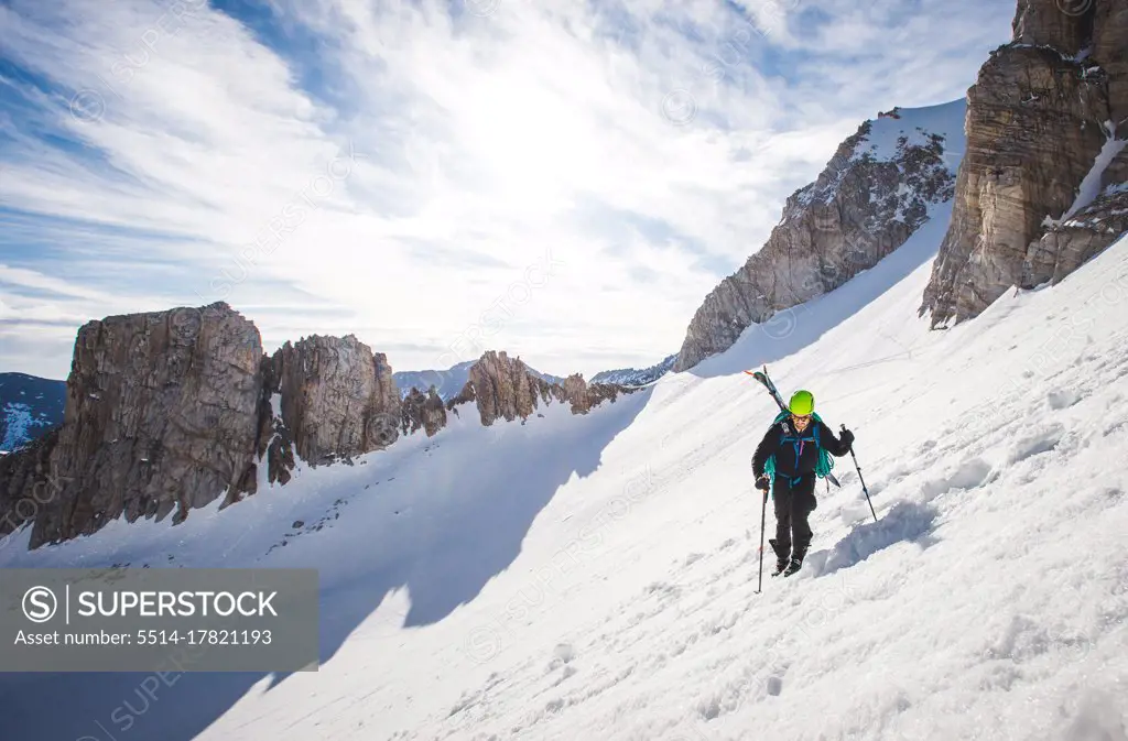 Man walking up steep snow section in California backcountry with skis