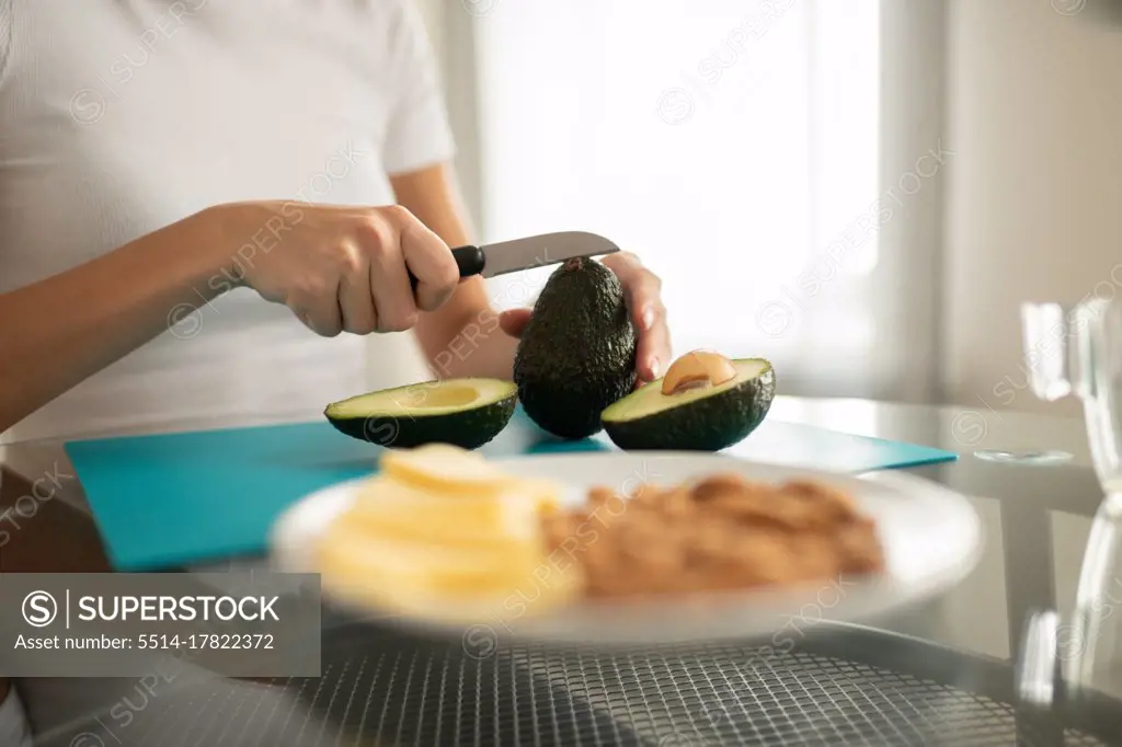 Crop woman cutting ripe avocado at table